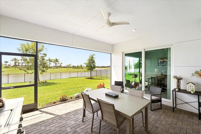 sunroom featuring a ceiling fan, a water view, and outdoor dining space