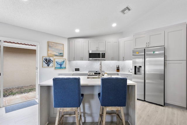 3773 NW 63rd Ct, Coconut Creek, FL 33073 - kitchen featuring visible vents, stainless steel appliances, a center island with sink, tasteful backsplash, and light wood-type flooring