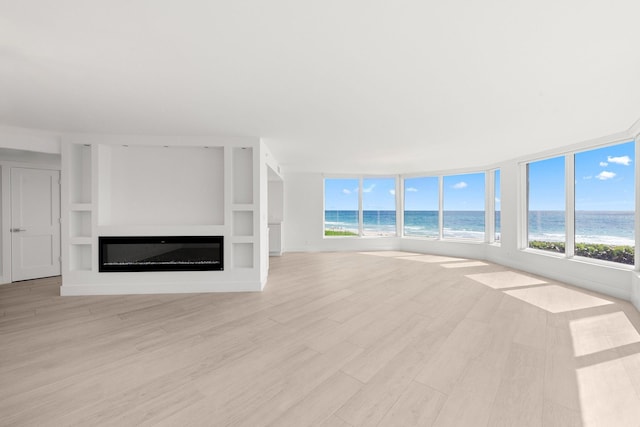2575 S Ocean Blvd Unit 102S, Highland Beach, FL 33487 - unfurnished living room featuring a glass covered fireplace, light wood-style floors, and a water view