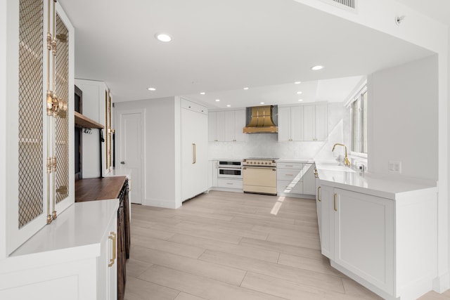 kitchen featuring white appliances, recessed lighting, wall chimney exhaust hood, tasteful backsplash, and a sink