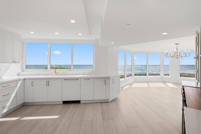 kitchen featuring an inviting chandelier, a water view, light wood-style floors, and white cabinetry