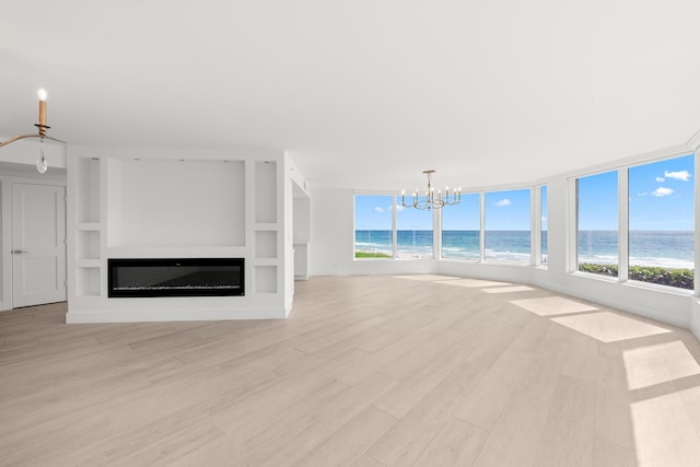 unfurnished living room featuring light wood finished floors, a glass covered fireplace, a notable chandelier, and a healthy amount of sunlight