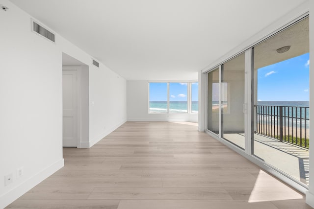 unfurnished room featuring a beach view, a water view, light wood finished floors, and visible vents