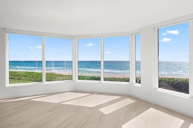 unfurnished sunroom featuring a water view, wood finished floors, and a beach view