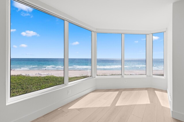 unfurnished sunroom featuring a water view, a wealth of natural light, and a beach view