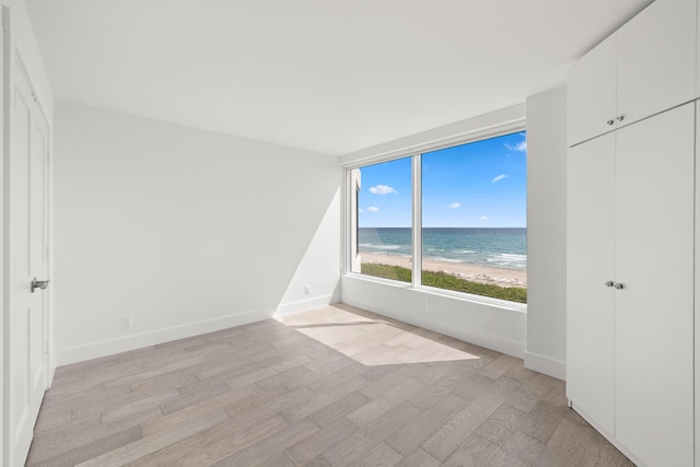 empty room with baseboards, light wood finished floors, and a water view