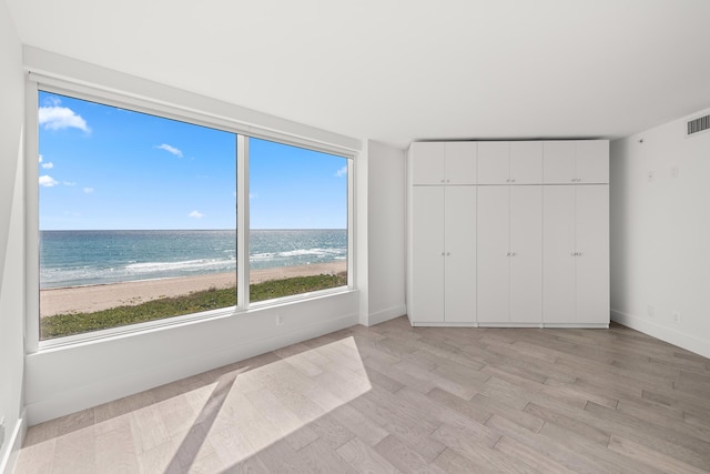 unfurnished bedroom with baseboards, a water view, light wood-style flooring, and visible vents