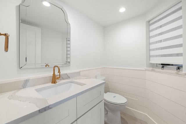 bathroom with recessed lighting, toilet, a wainscoted wall, and vanity