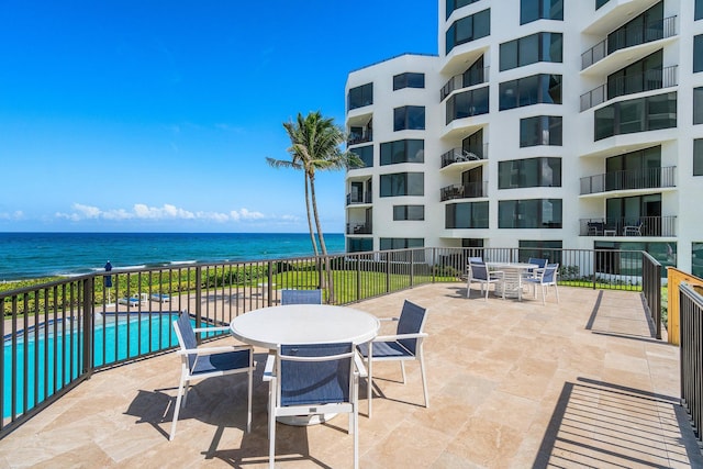 view of patio / terrace with a water view, outdoor dining area, fence, and a community pool