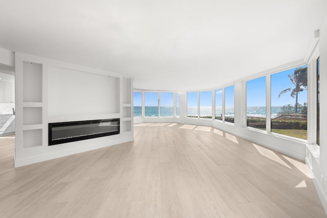 2575 S Ocean Blvd Unit 102S, Highland Beach, FL 33487 - unfurnished living room featuring a water view, a glass covered fireplace, and light wood-style floors