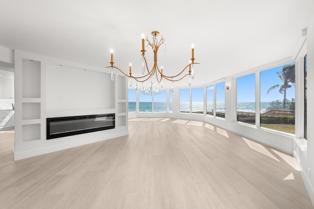 interior space with an inviting chandelier, light wood-style floors, a water view, and a healthy amount of sunlight