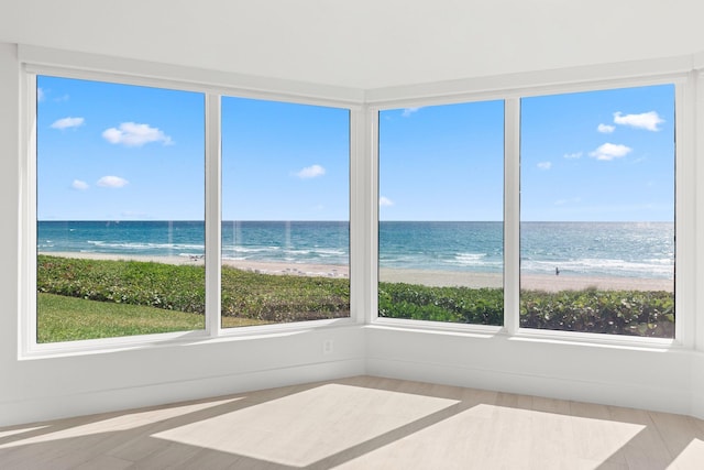 unfurnished sunroom with a water view, wood finished floors, and a view of the beach