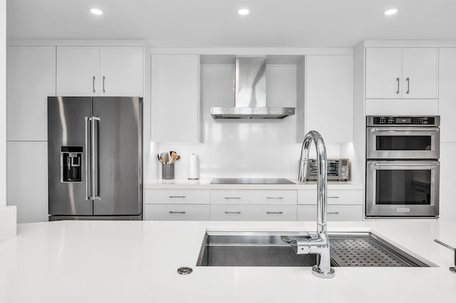 kitchen featuring appliances with stainless steel finishes, wall chimney exhaust hood, recessed lighting, light countertops, and a sink