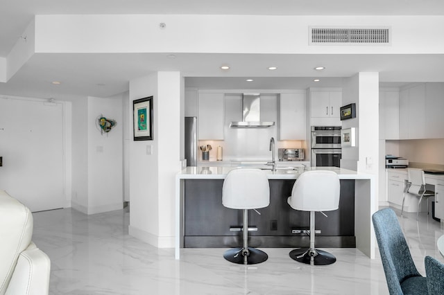 kitchen with modern cabinets, wall chimney exhaust hood, light countertops, a breakfast bar, and white cabinetry