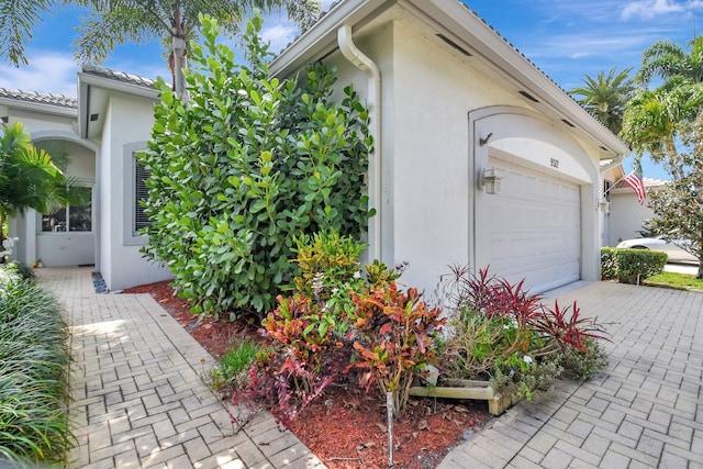 view of side of home with an attached garage, driveway, and stucco siding