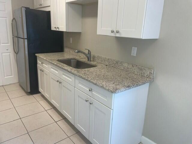 6881 Church St, Jupiter, FL 33458 - kitchen featuring a sink, freestanding refrigerator, light stone countertops, light tile patterned floors, and white cabinets
