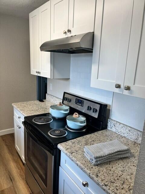6881 Church St, Jupiter, FL 33458 - kitchen featuring white cabinetry, stainless steel range with electric stovetop, baseboards, under cabinet range hood, and wood finished floors