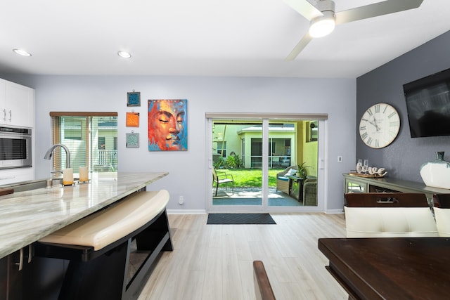 kitchen featuring a sink, white cabinetry, light stone countertops, stainless steel oven, and light wood-style flooring