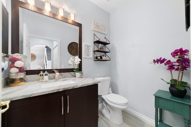 half bathroom featuring vanity, baseboards, and toilet