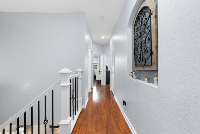 hall featuring a textured wall, an upstairs landing, baseboards, and wood finished floors