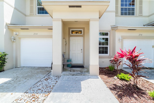 doorway to property featuring concrete driveway, stucco siding, visible vents, and an attached garage