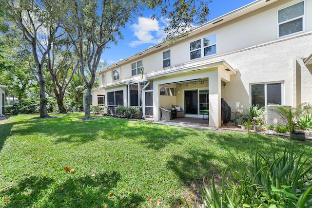 back of property featuring a patio, stucco siding, a sunroom, and a lawn