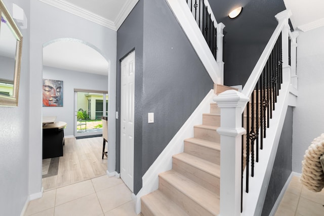 staircase with arched walkways, tile patterned floors, baseboards, and ornamental molding