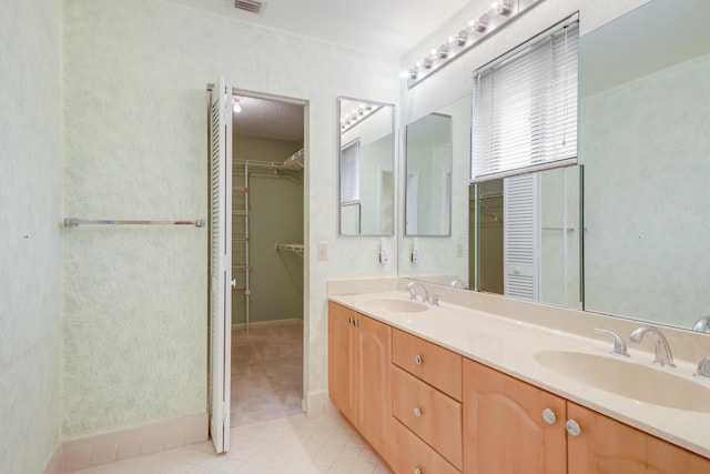 full bathroom with baseboards, double vanity, a walk in closet, and a sink