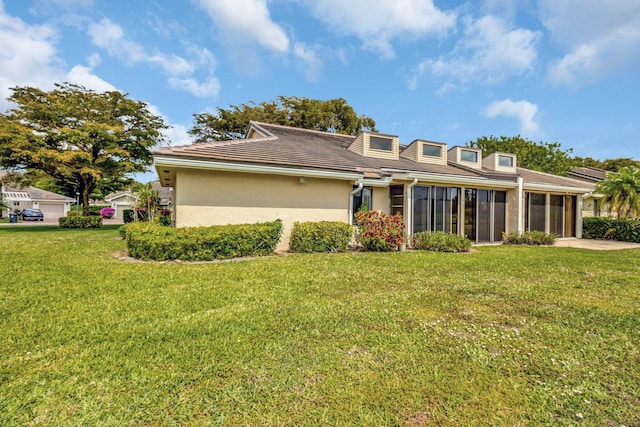 rear view of property featuring a yard, an attached garage, a sunroom, and stucco siding