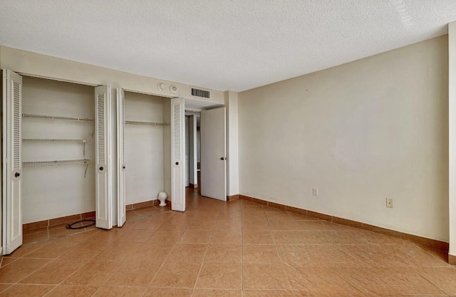 unfurnished bedroom featuring multiple closets, a textured ceiling, light tile patterned flooring, and baseboards