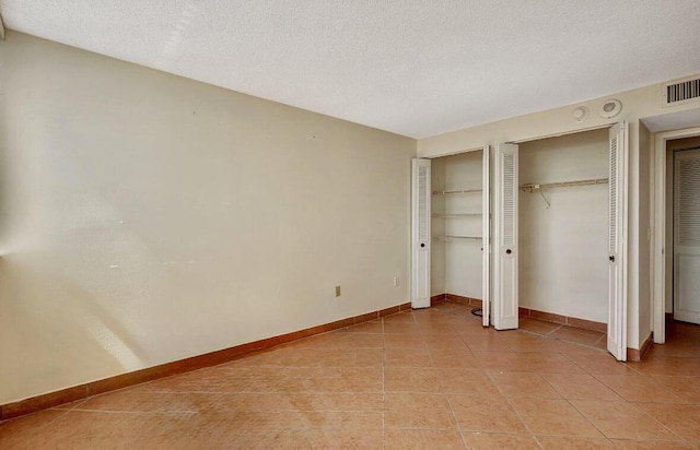 unfurnished bedroom featuring multiple closets, light tile patterned floors, baseboards, and a textured ceiling
