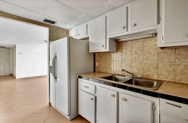 kitchen featuring a sink, white cabinetry, white fridge with ice dispenser, light tile patterned floors, and a paneled ceiling