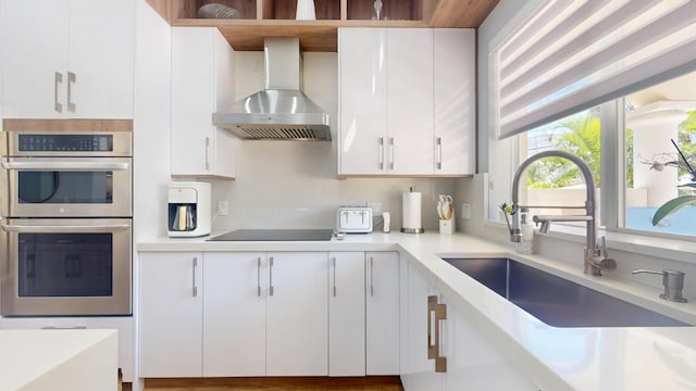 1942 NE 6th St, Deerfield Beach, FL 33441 - kitchen featuring a sink, stainless steel double oven, black electric cooktop, wall chimney range hood, and white cabinets