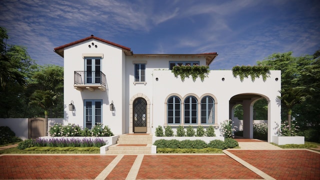 mediterranean / spanish-style house featuring fence, french doors, a balcony, and stucco siding