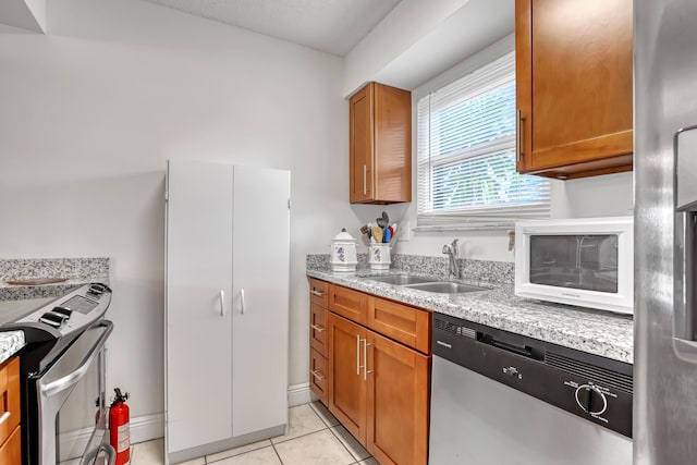 kitchen featuring light stone countertops, a sink, stainless steel appliances, and brown cabinets