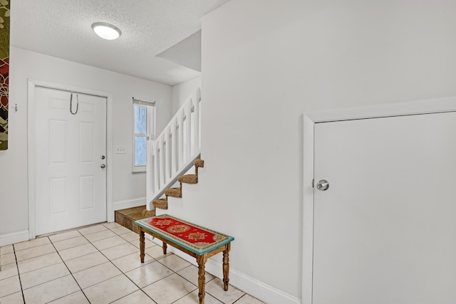 entrance foyer with light tile patterned flooring, baseboards, stairway, and a textured ceiling