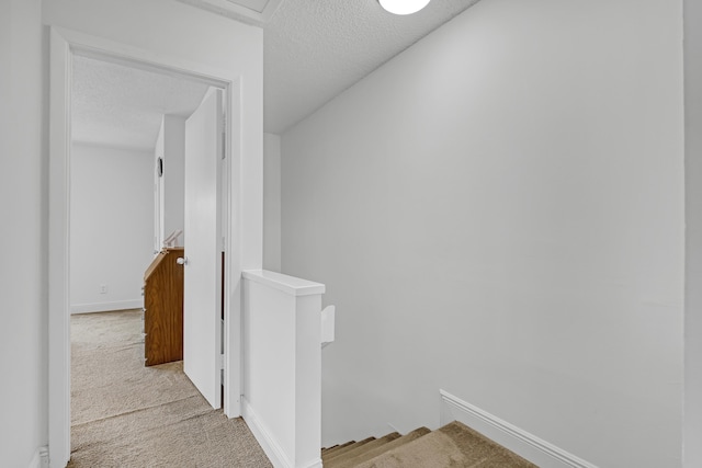 corridor featuring a textured ceiling, an upstairs landing, baseboards, and carpet