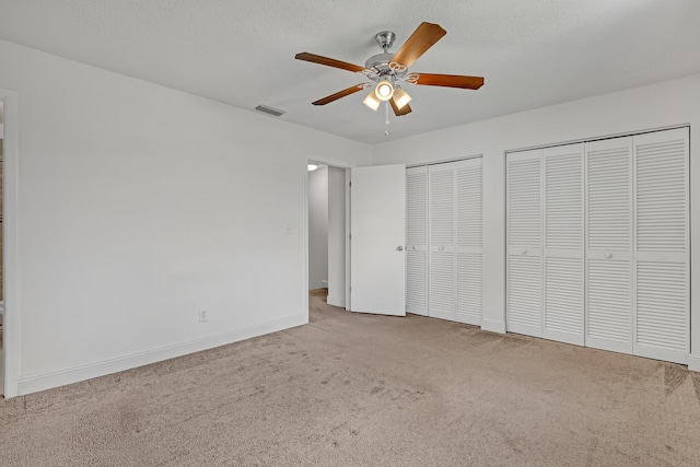 unfurnished bedroom with carpet flooring, a textured ceiling, visible vents, two closets, and baseboards