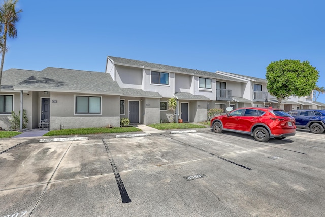 multi unit property with a residential view, stucco siding, uncovered parking, and a shingled roof