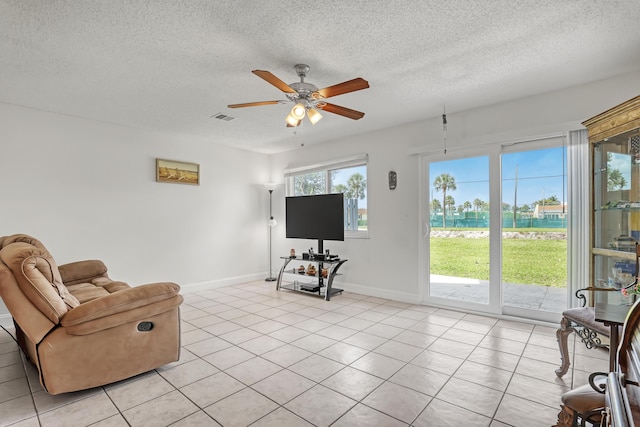 living area with a ceiling fan, a textured ceiling, light tile patterned floors, baseboards, and visible vents