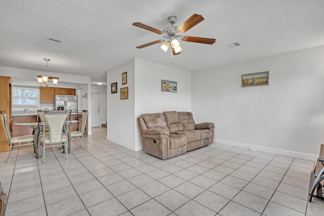 living room with light tile patterned flooring, a textured ceiling, visible vents, and ceiling fan with notable chandelier