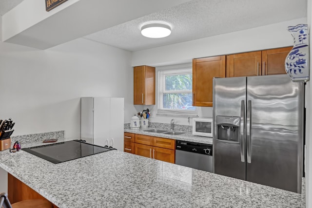kitchen featuring a textured ceiling, a sink, brown cabinetry, and appliances with stainless steel finishes