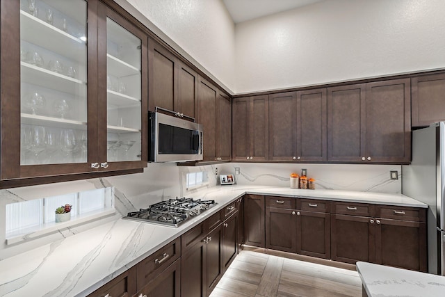 149 Sedona Way, Palm Beach Gardens, FL 33418 - kitchen with stainless steel appliances, dark brown cabinetry, light stone counters, and glass insert cabinets
