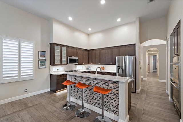 149 Sedona Way, Palm Beach Gardens, FL 33418 - kitchen with stainless steel appliances, dark brown cabinetry, a towering ceiling, a kitchen island with sink, and baseboards