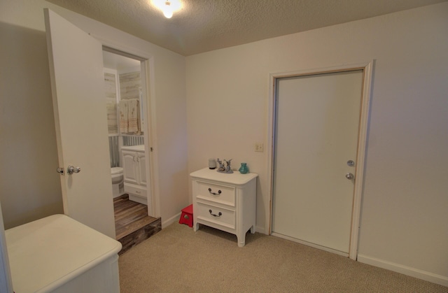 interior space featuring baseboards, a textured ceiling, connected bathroom, and light carpet