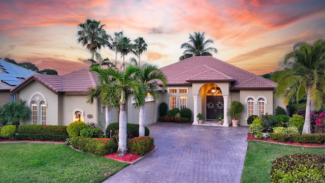mediterranean / spanish home with stucco siding, a tiled roof, driveway, a garage, and a yard