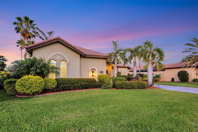 mediterranean / spanish house featuring stucco siding, a tiled roof, and a yard