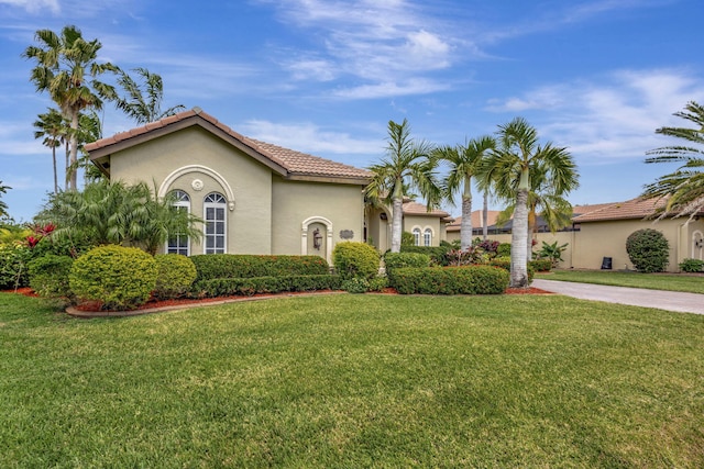 mediterranean / spanish home with stucco siding, driveway, a tiled roof, and a front yard