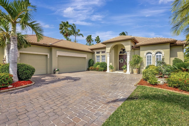 mediterranean / spanish home featuring stucco siding, a garage, a tiled roof, and decorative driveway