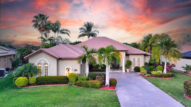mediterranean / spanish home with a lawn, a tile roof, decorative driveway, and stucco siding